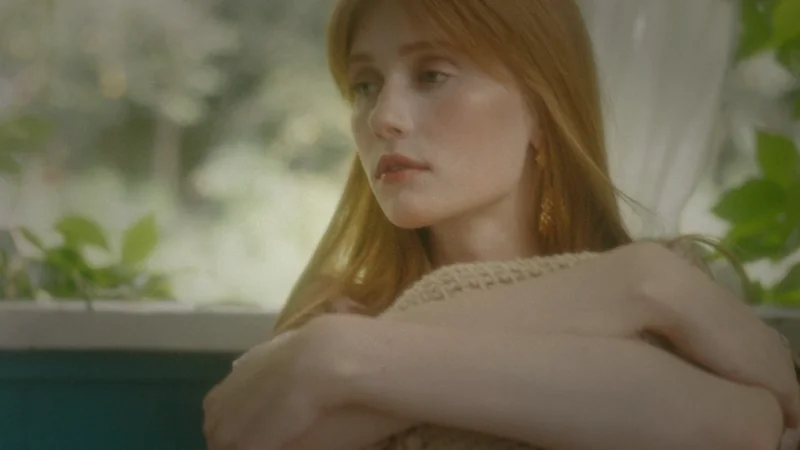 A calm-looking woman sits by a bright window holding her arms close to her body, illustrating physical anxiety without obvious anxious thoughts